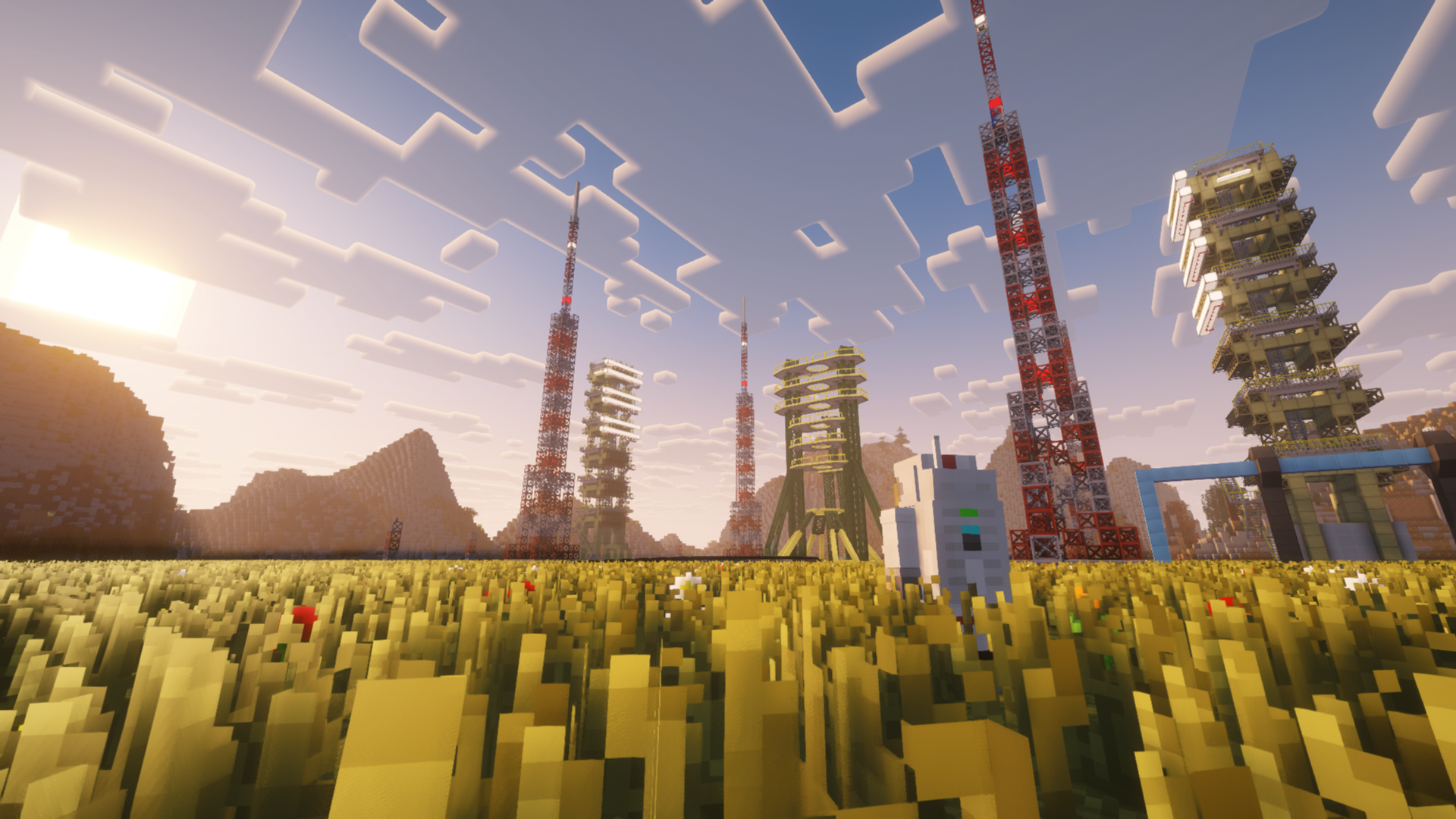 Launch gantries and tall red-and-white towers rise above a grassy field beneath a bright, cloud-filled sky.